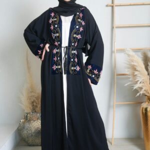 Stylish woman in embroidered black hijab abaya, standing in a chic indoor setting.