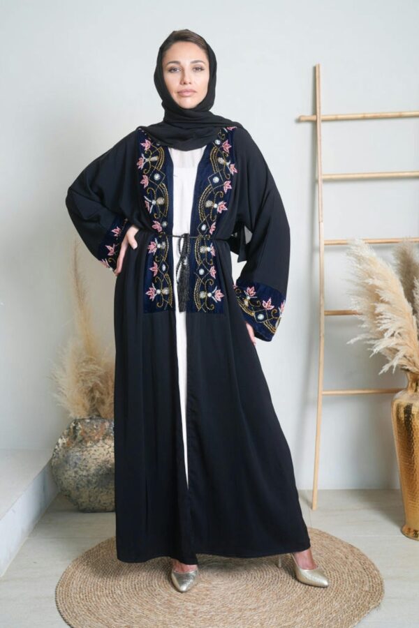 Stylish woman in embroidered black hijab abaya, standing in a chic indoor setting.